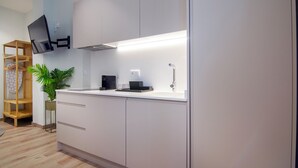 Una cocina moderna con armarios blancos, un microondas integrado y un televisor de pantalla plana montado en la pared.