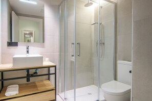 A modern bathroom with a glass-enclosed shower, a white sink, and a wooden vanity. - VLC HOST - Reino 7 (Valencia)