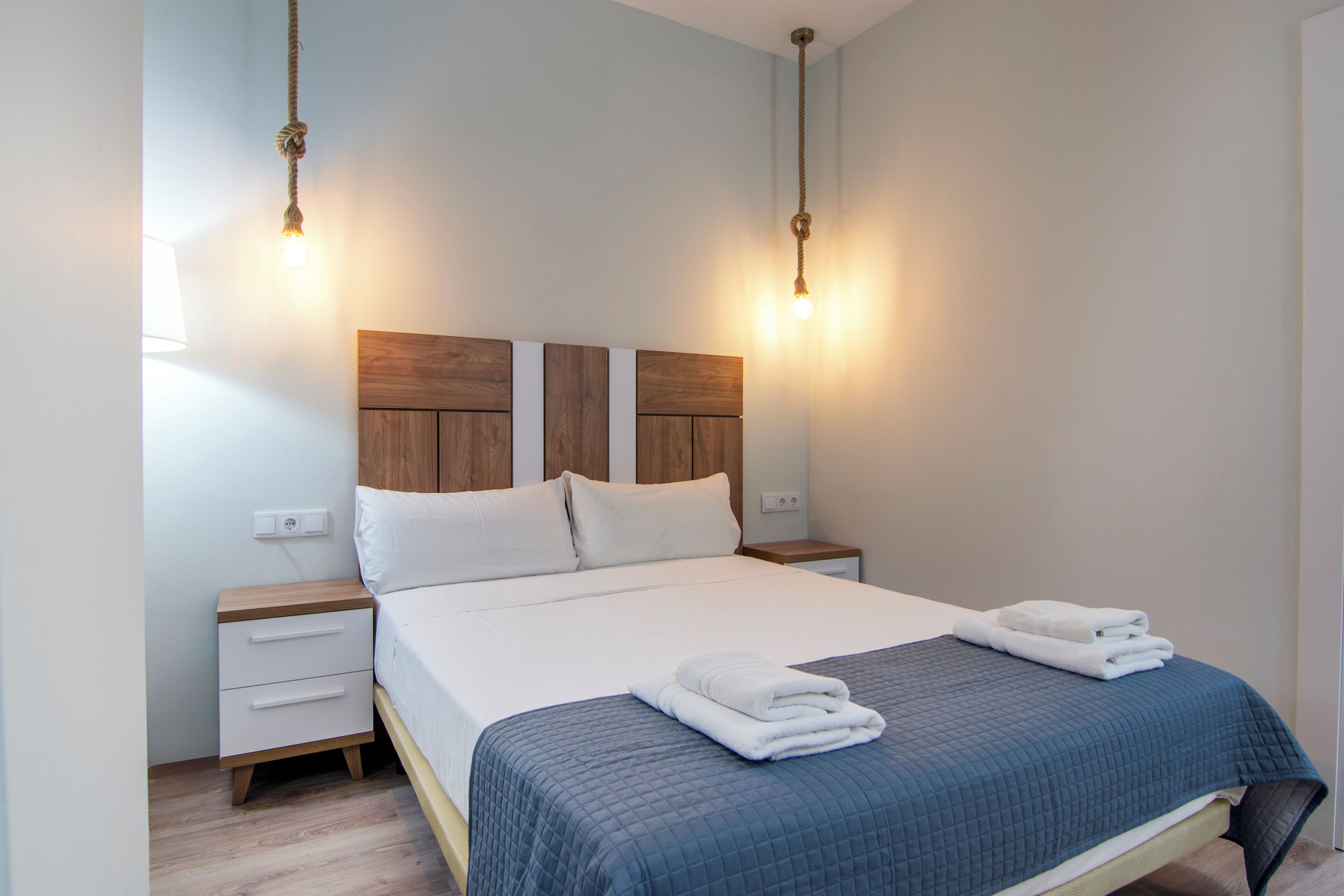 A neatly made bed with a blue quilt, two bedside tables with wooden tops, and two wall-mounted lights.
