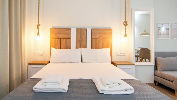 Habitación de hotel con una cama grande, dos mesitas de noche, un cabecero de madera y una ventana con vista al cuarto.