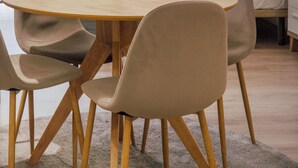 Un comedor moderno con una mesa redonda de madera y cuatro sillas, una lámpara colgante, y vistas a un dormitorio con cama y cortinas.