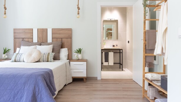 A bedroom with a bed, bedside tables, a nightstand, a wooden wardrobe, a bathroom with a mirror, and a hanging plant. - VLC HOST - Reino 9 (Valencia)