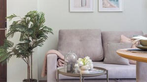 A living room with a grey sofa, a small round table with a glass top, a potted plant, and two framed pictures on the wall. - VLC HOST - Reino 9 (Valencia)