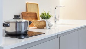 A modern kitchen with a stainless steel pot on an induction cooktop, a wooden cutting board, a potted plant, and a sleek faucet. - VLC HOST - Reino 9 (Valencia)