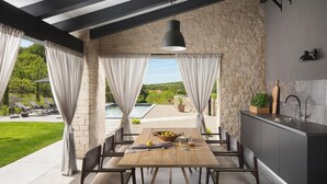 Une cuisine moderne avec un mur en pierre, un coin repas avec une table et des chaises en bois, et une vue sur une piscine et un espace verdoyant.