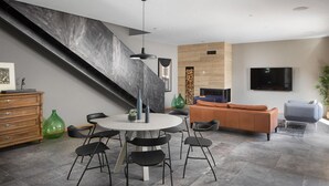 Un salon moderne avec une table à manger ronde, des chaises noires, un canapé et un téléviseur fixé au mur.