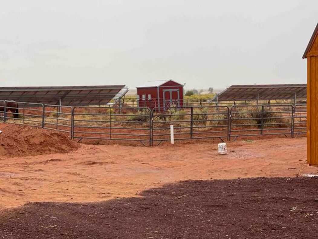 A fenced area with solar panels, a red building, and a wooden structure.