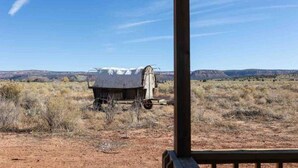 Una estructura rústica al aire libre con un área techada, frente a un paisaje seco y montañoso bajo un cielo despejado.