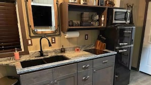 Una cocina con encimera de granito, armarios oscuros, microondas integrado y pileta de acero inoxidable.