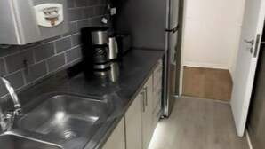 Una cucina angusta con mobili grigi, un lavello in acciaio inossidabile e un frigorifero.