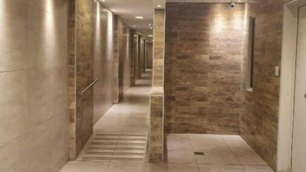 Un corridoio con pavimento e pareti piastrellate, caratterizzato da una colonna centrale e porte su entrambi i lati.