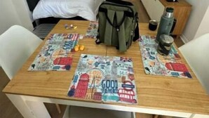 Una camera d'albergo compatta con un letto, una scrivania con una mappa, uno zaino e una TV.