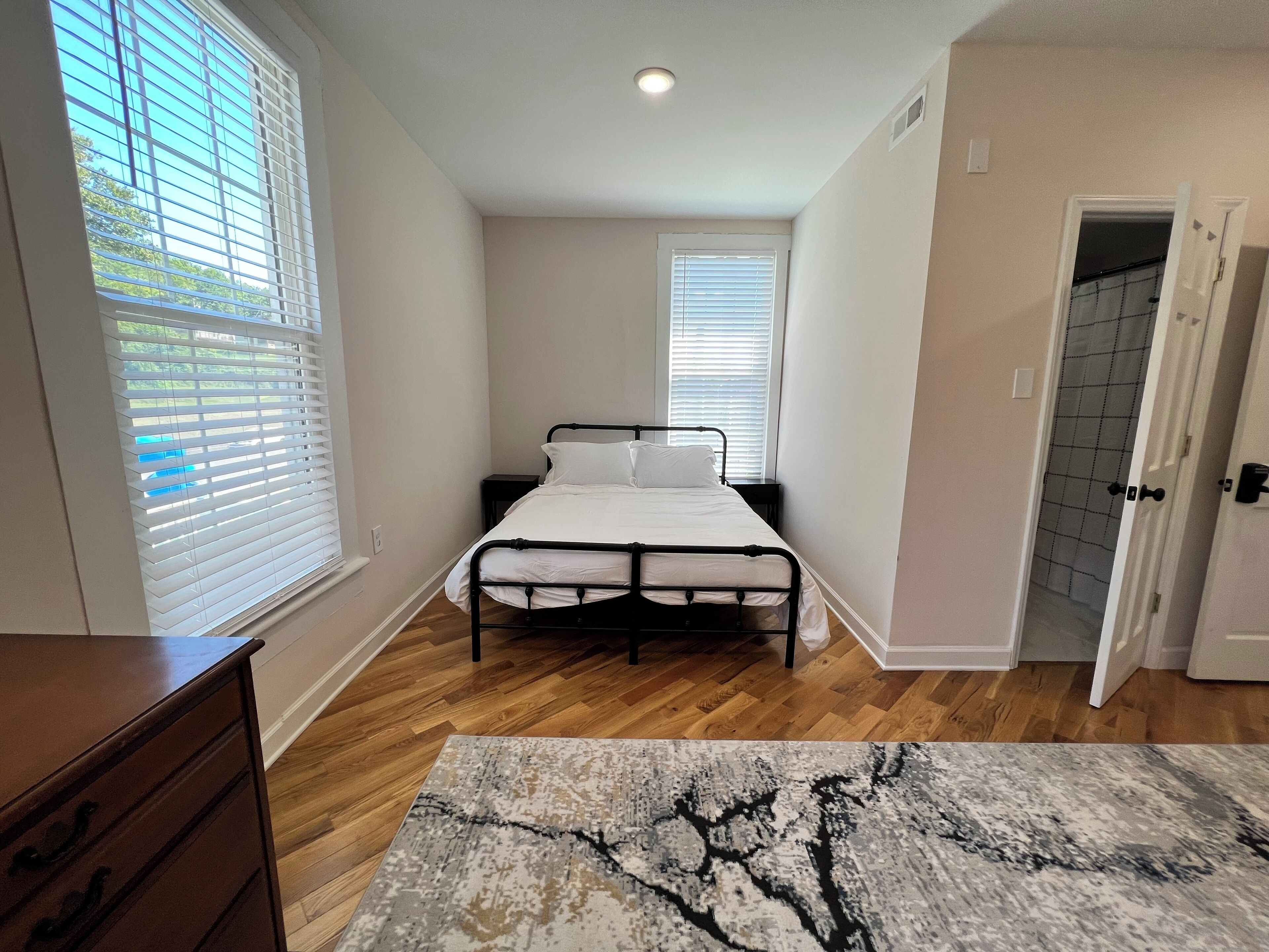 A bedroom with a bed, wooden floor, and a view of the outside through the window.
