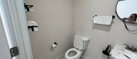 Un baño con inodoro, lavamanos, espejo y toallero.