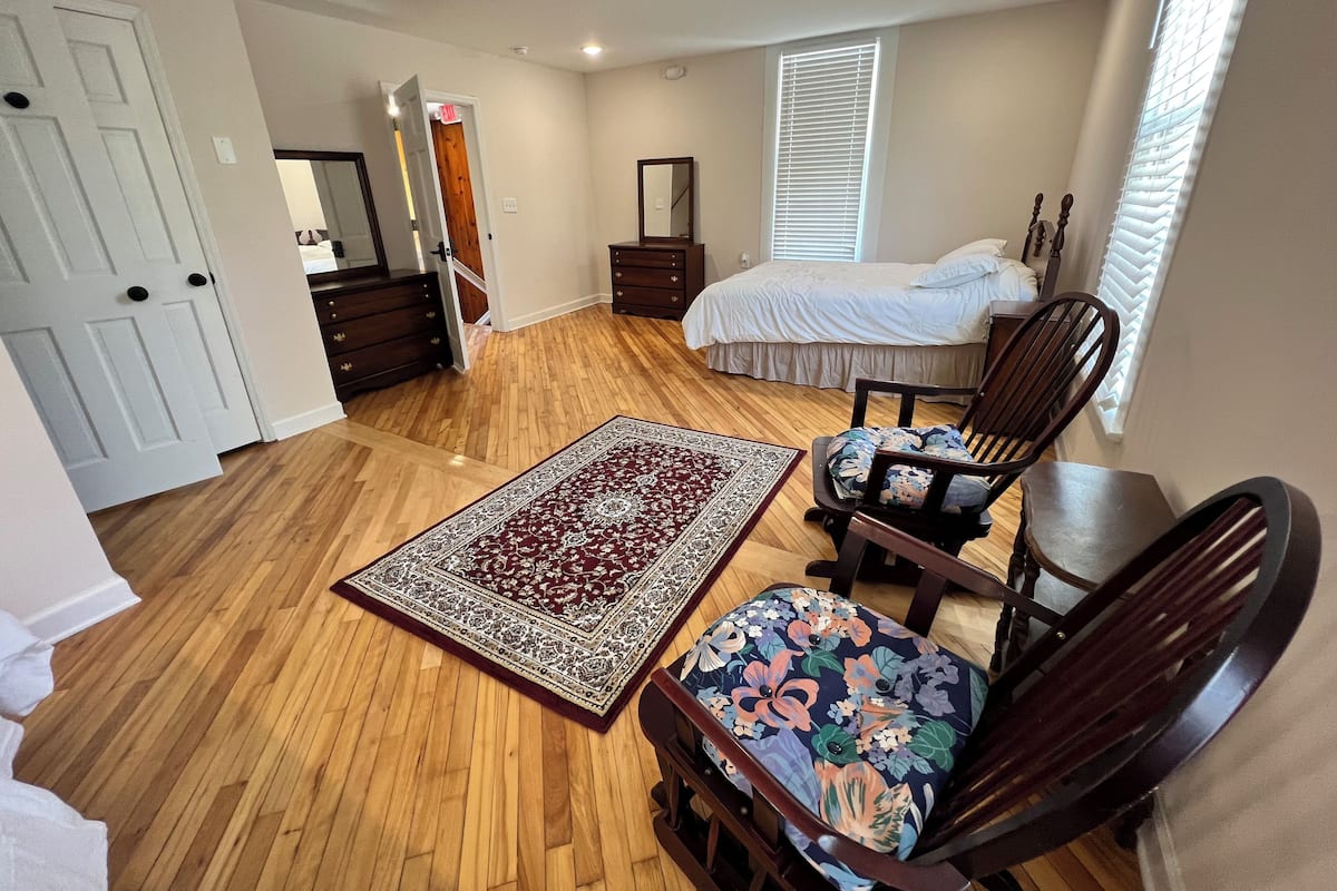 A bedroom with a wooden floor, a bed, a chair, a dresser, and a nightstand.