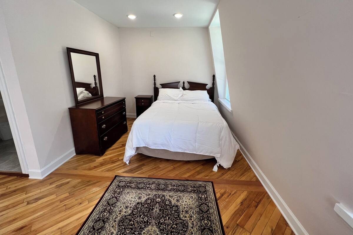 A bedroom with a bed, dresser, mirror, and a patterned rug.