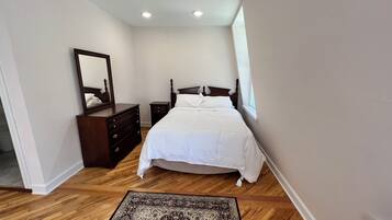 Un dormitorio con cama, cómoda, espejo y una alfombra estampada.