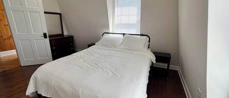 Een slaapkamer met een bed, nachtkastje, dressoir, raam en deur.