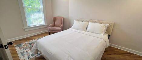 A bedroom with a large bed, a chair, a window with blinds, and a patterned rug.