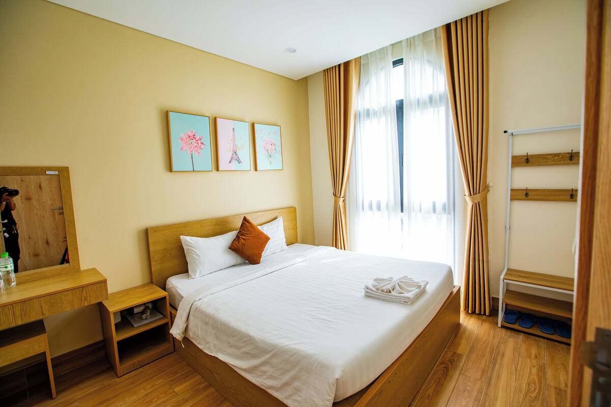 Ein Hotelzimmer mit einem hölzernen Bett, einem Nachttisch, einem Spiegel und einem Fenster mit Vorhängen.