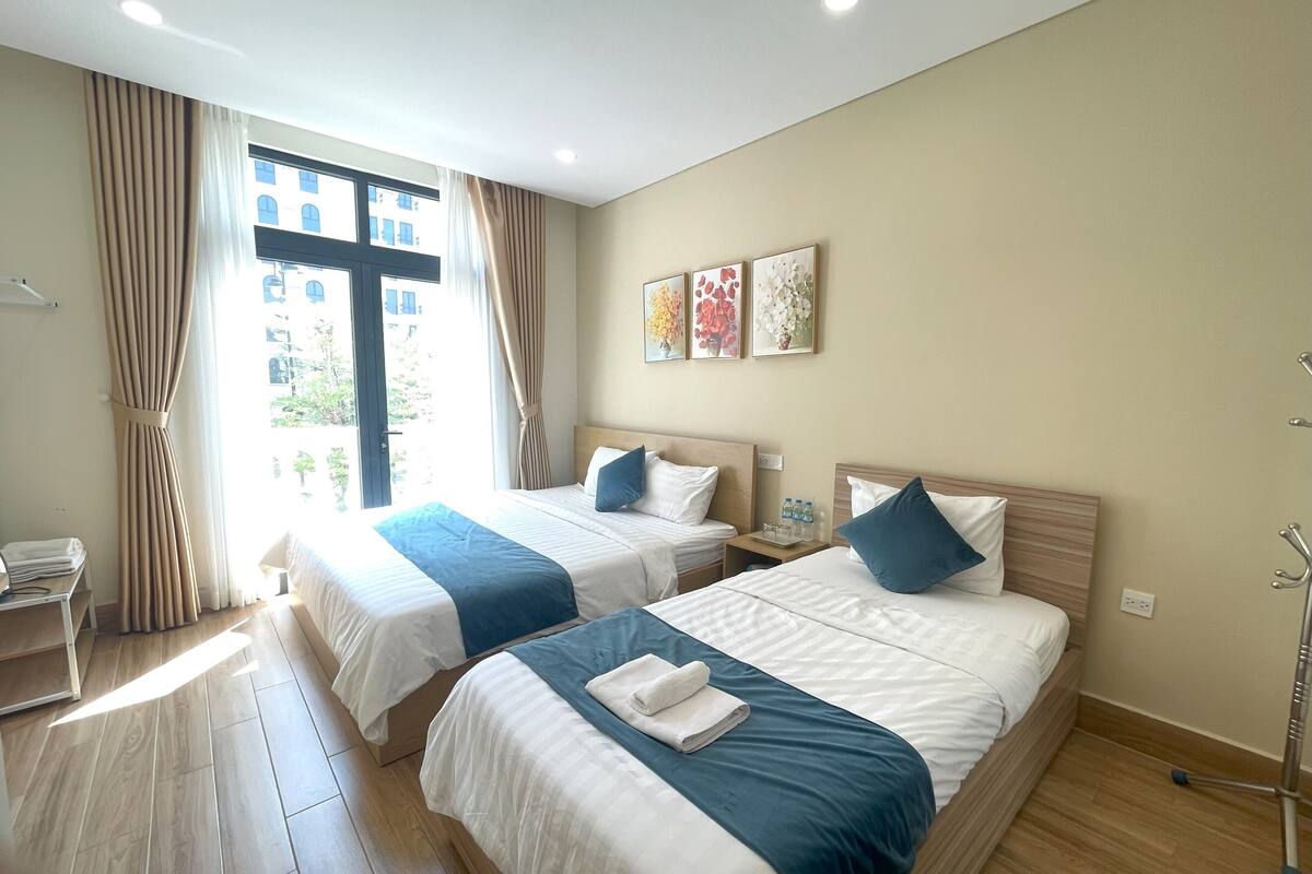Ein Hotelzimmer mit zwei Betten, einem Schreibtisch und einem Fenster mit Vorhängen.