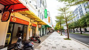Un trottoir bordé de boutiques, dont un café et un salon de thé, avec des arbres et un ciel dégagé en arrière-plan.