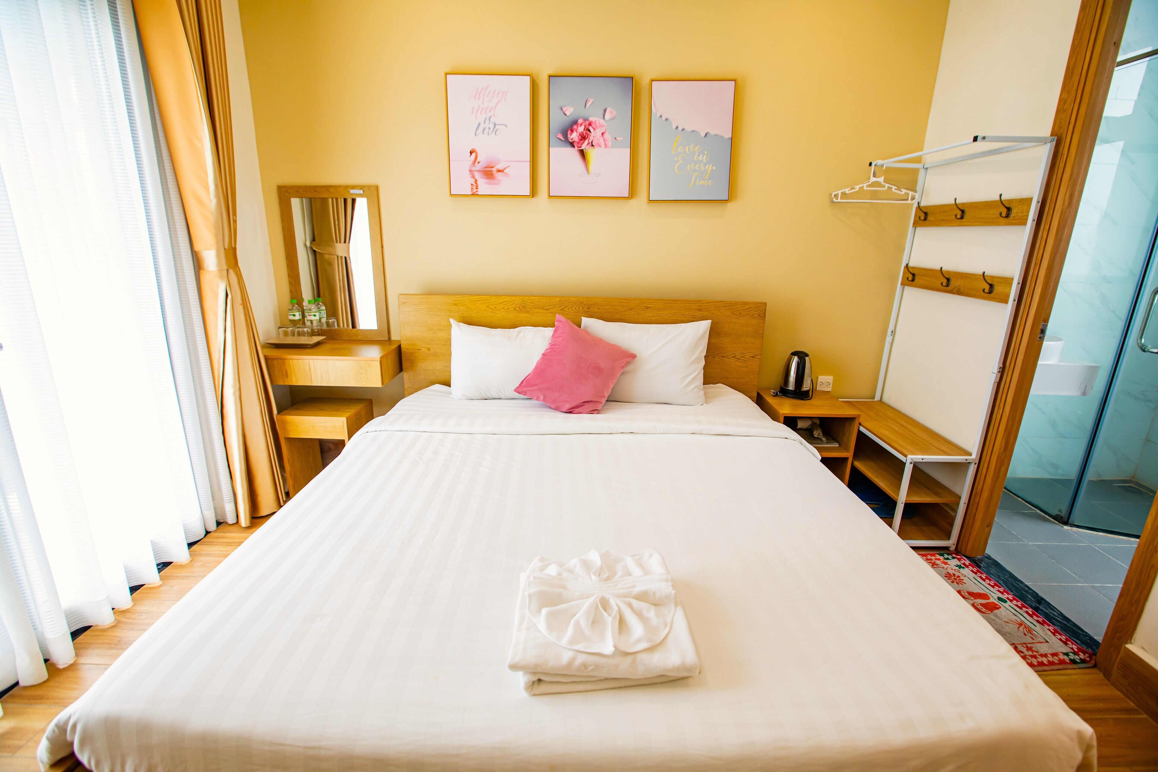 A hotel room with a large bed, a wooden nightstand, a mirror, and a wall with three framed pictures.