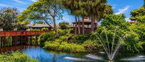 A serene garden with a pond, a wooden bridge, and a gazebo.