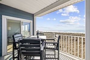 Un espace extérieur abrité, équipé d’une table et de chaises, avec une bouteille et un verre, donnant sur une plage.