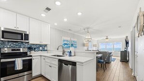 Una cocina moderna con armarios blancos, electrodomésticos de acero inoxidable y vista al océano.