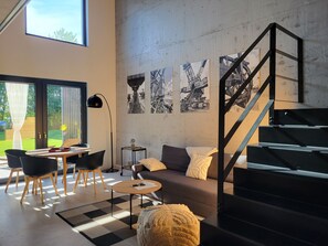 Un salon moderne avec un escalier, un canapé, une table basse et un coin repas avec des chaises.