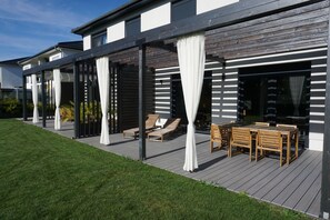A modern outdoor patio with wooden furniture and white curtains.