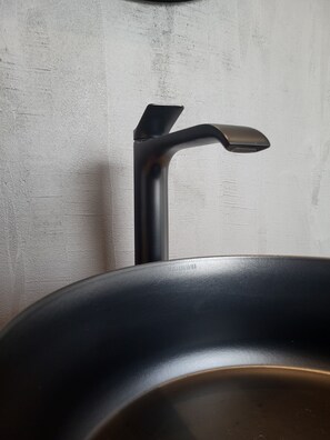 Un lavabo de salle de bain doté d’un robinet moderne et d’un bac de couleur sombre.