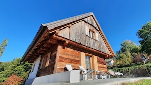 A wooden cabin with a sloped roof, a large window, and a balcony with outdoor seating.