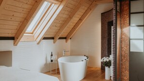 A modern bathroom with a freestanding bathtub, a small table with a bottle and glass, and a white rug on the floor.