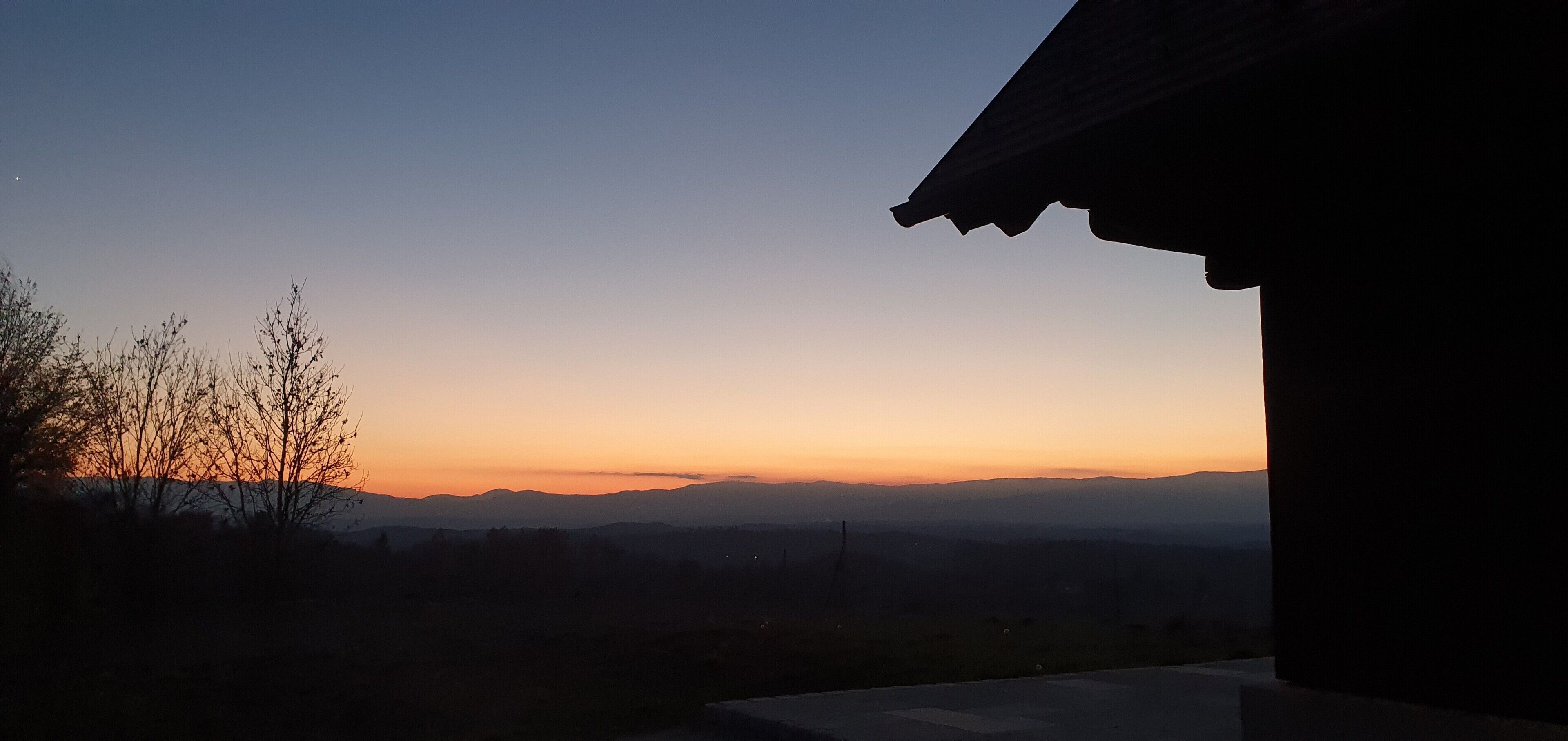 A sunset view from a building with a roof visible on the right.