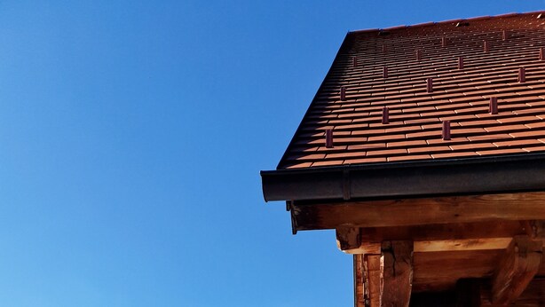 A wooden building with a tiled roof, a covered outdoor seating area with chairs, and a view of distant mountains.