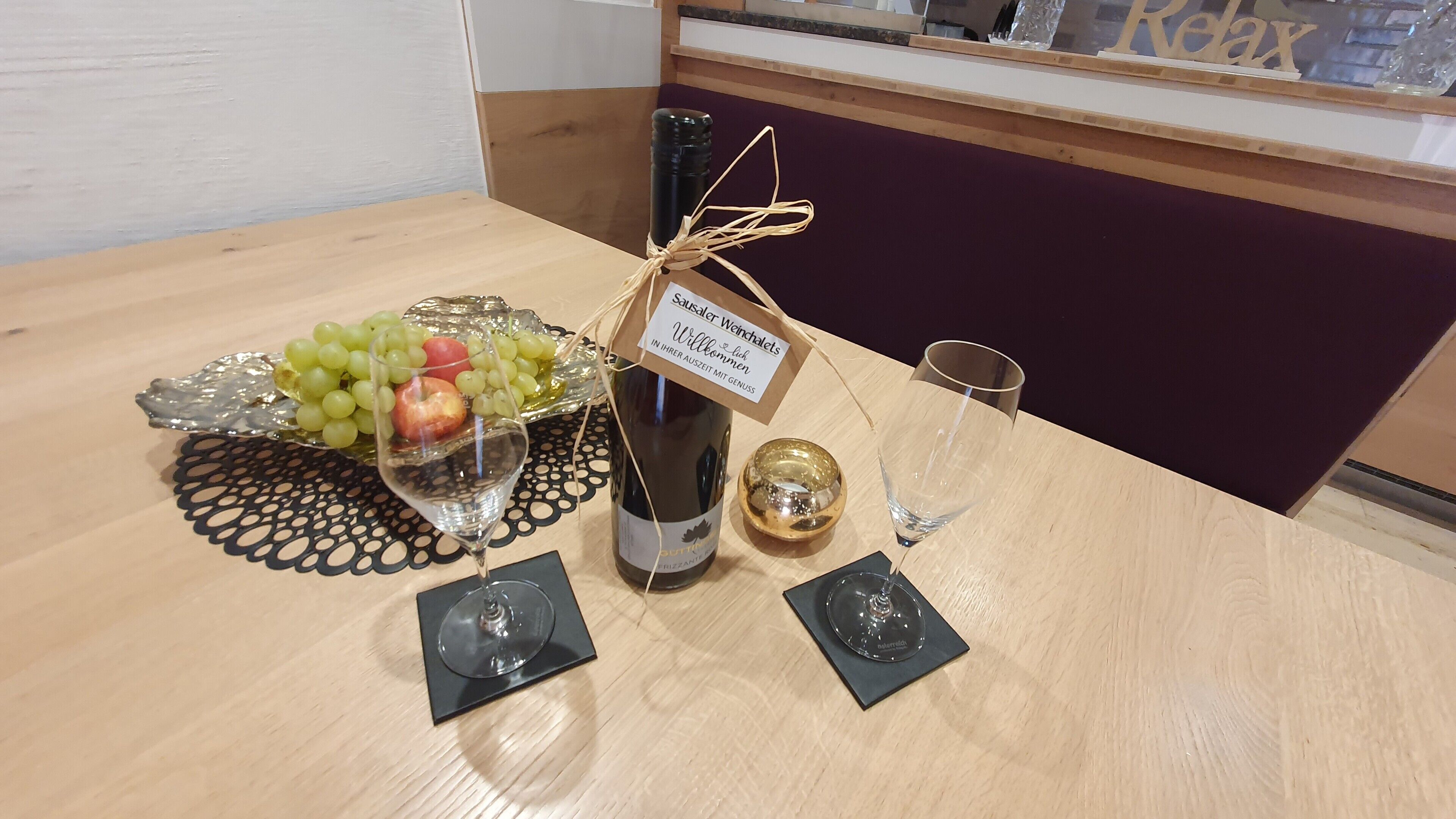 A table with a bottle of wine, a glass of wine, a glass of water, a bowl of grapes, and a decorative item.