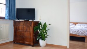 A room with a wooden dresser, a potted plant, a bed with a floral bedspread, and a window with blue curtains. - Mercyscher Hof Apartment, 70 sqm, 2 Bedrooms, 1 Living Room, up to 6 Guests (Gengenbach)