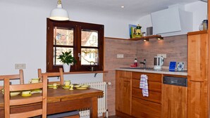 A kitchen with wooden cabinets, a dining table with chairs, a window with a plant, and a hanging light fixture.
