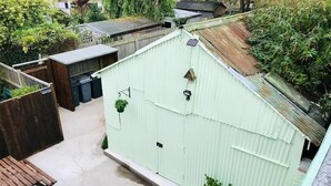 A small, enclosed outdoor space with a concrete floor, a wooden bench, and a corrugated metal shed. - Modern & Brand New Apartment in Whitstable Centre (Whitstable)
