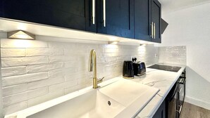 A modern kitchen with dark cabinets, a white countertop, and a stainless steel sink. - Modern & Brand New Apartment in Whitstable Centre (Whitstable)