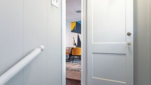 Un pasillo con una puerta blanca, una barandilla blanca y un comedor con una mesa y sillas.