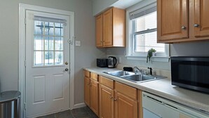 Una cocina con armarios de madera, un lavamanos de acero inoxidable, un microondas y una ventana con persianas.