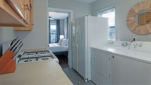 Cocina compacta con estufa a gas, refrigerador y lavadora. Se ve una cama a través de una puerta abierta en la habitación contigua.