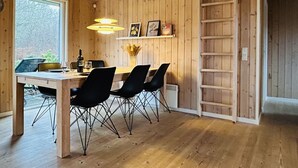 A wooden interior with a dining table, chairs, pendant lights, a ladder, and a window.