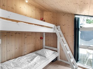 A bunk bed room with wooden walls, a ladder, and a window with a view of the outside.