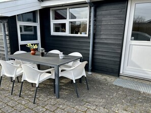 An outdoor dining area with a table and chairs, a coffee pot, and a vase with flowers.