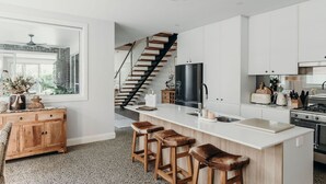 A modern kitchen with a central island, bar stools, a refrigerator, and a staircase leading to another level. - Gypsea at the Bay, 26b Achilles St - Wi-Fi , air con, luxury and linen (Nelson Bay)