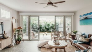 A spacious living room with a large sliding glass door leading to a garden, a ceiling fan, and a view of the outdoors. - Gypsea at the Bay, 26b Achilles St - Wi-Fi , air con, luxury and linen (Nelson Bay)